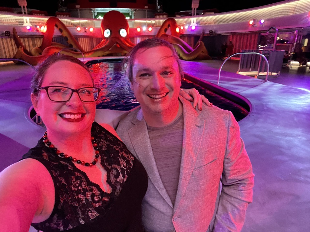 Wife and I in front of the pool and a large orange octopus. She is without sleeves and I am wearing a blazer. It was too hot!